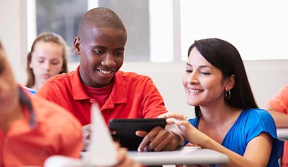 Teacher happily helping student with their digital device in class.