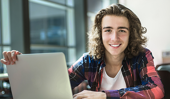 about-research-report Young man smiling whilst working on his laptop.