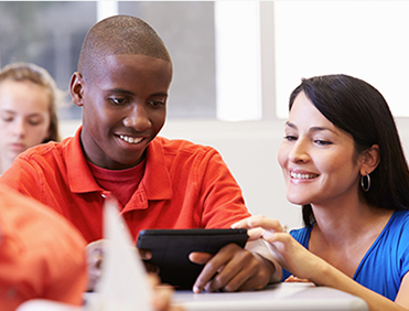 Teacher happily helping student with their digital device in class.