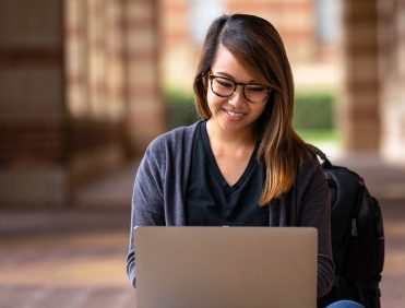 A young woman happily working on her laptop outdoors.