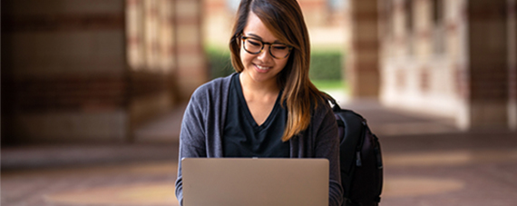 A young woman happily working on her laptop outdoors.