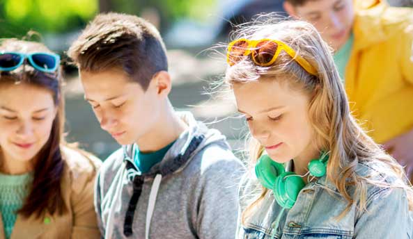 impactreport2020 Group of three students enjoying their digital devices outdoors.