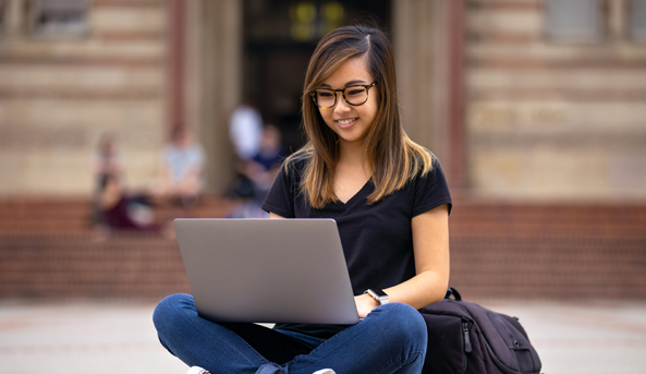 A young woman happily working on her laptop outdoors.