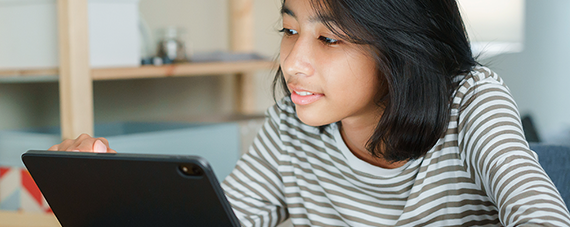 570x227 Young girl smiling at what she is watching on her iPad.