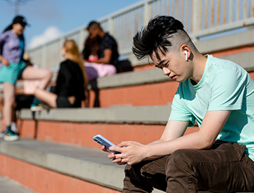 Teen boy using smartphone alone away from friends