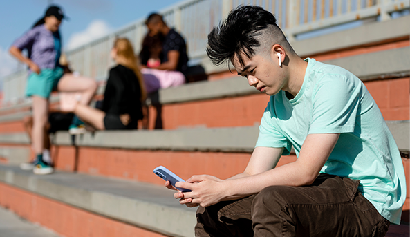 Teen boy using smartphone alone away from friends Teen boy using smartphone alone away from friends