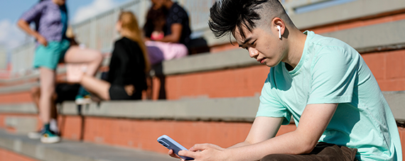 Teen boy using smartphone alone away from friends