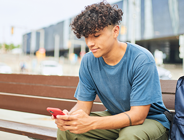 Young boy sitting on a city bench talking on a mobile phone