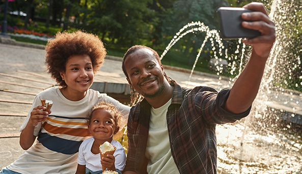 A young man, his sister and father take a selfie together outside whilst holding icecream cones.