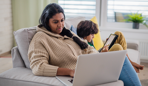 A woman contently looking at her laptop with her child beside her.