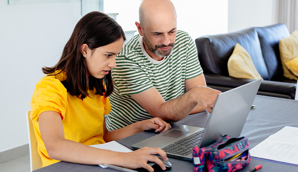 A young woman and her father converse whilst looking at a laptop.