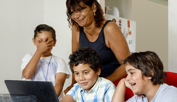 Three young boys and their mother enjoying an activity together on a laptop.
